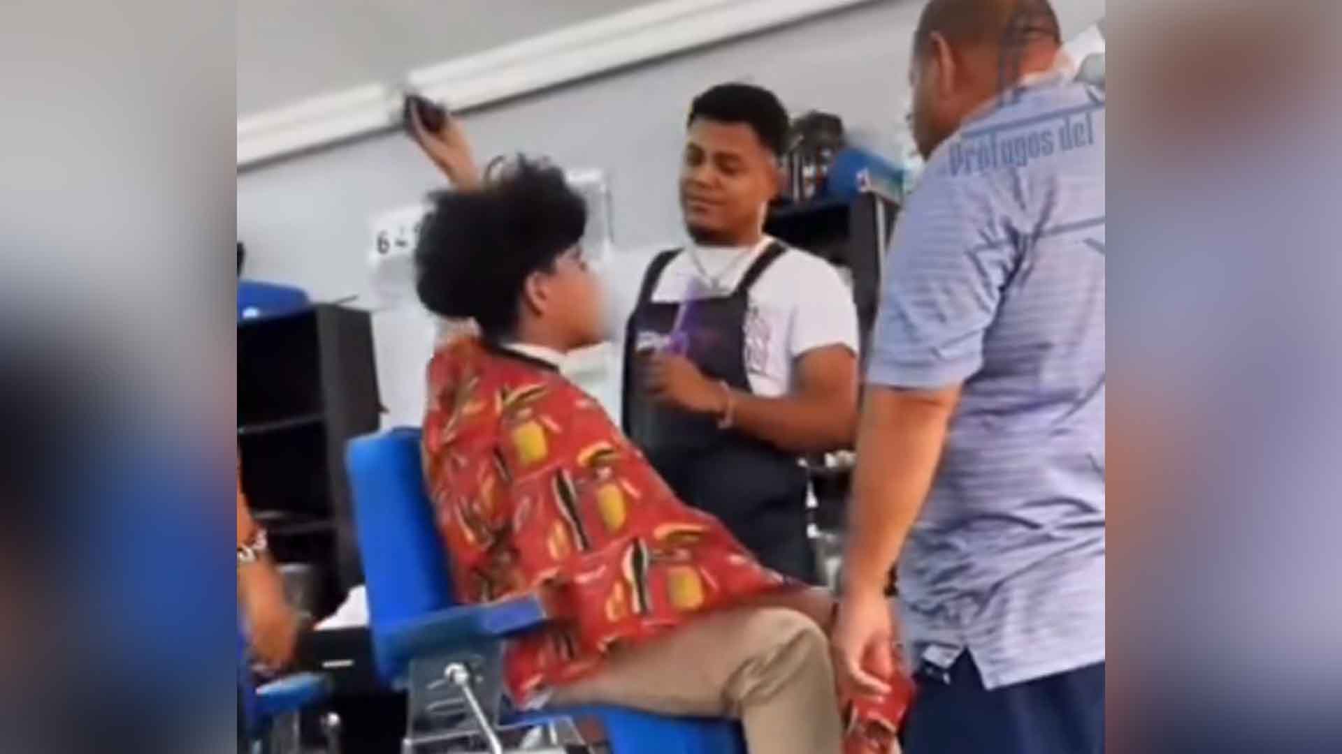 Momento en el que el padre le entrega las indicaciones al peluquero que cortará el cabello de su hijo