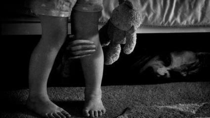Una bruja se oculta debajo de una cama y sujeta el pie de una niña. 