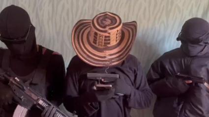 Imagen de los sujetos que aparecen armados y leen el mensaje desde un teléfono celular.